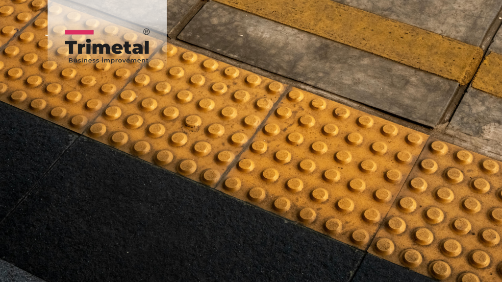 Modern bir bina girişinde, görme engelli bireyin beyaz bastonuyla dokunduğu, paslanmaz çelikten yapılmış Trimetal hissedilebilir takip ve uyarı yüzeyi.